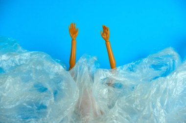 Plastik bebek elleri plastik torba yığınından sarkıyor, plastik içinde boğuluyor, küresel kirlilik çevre konsepti
