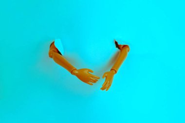 Plastik bir bebeğin elleri yırtık mavi kağıdı delip geçer yaratıcı minimalist natüralist hayat, turuncu ve deniz mavisi tonu