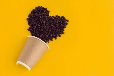 Üst kattaki düz kahve fincanı, kahve çekirdeğinden yapılmış kalp, sarı arka planda izole edilmiş kahve, kahve sevgisi ve kahve bağımlılığı kavramı.