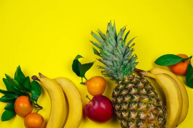 Üst manzara taze tropikal meyve düzeni ananas, muz, elma ve mandalina sarı arka planda.