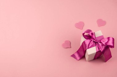 En üstteki hediye kutusunda saten kurdele yayı ve yumuşak pembe arka planda fotokopi alanı olan üç kalp var.