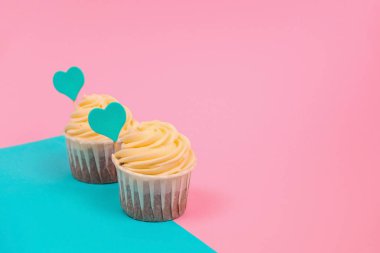 Mavi ve pembe arka plan fotokopi alanı üzerine mavi bir kalple süslenmiş tereyağı kremalı şirin kek.