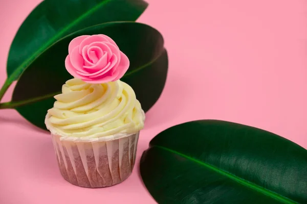 sweet cupcake decorated with roses and tropical leaves on a pastel pink background