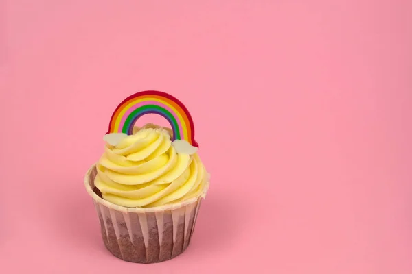 cupcake with butter cream decorated with rainbow figurine on a pastel pink background