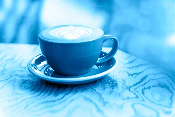 Mug biru cappuccino dengan busa susu di atas meja kayu kabur — Stok Foto
