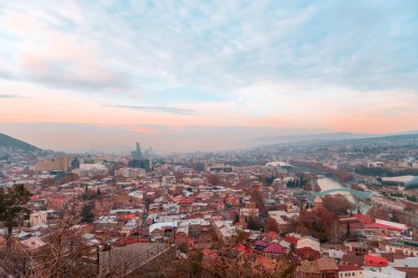 Tiflis, Gürcistan, 15 Aralık 2019 - Günbatımında şehir manzarasının arka planında kablo kamarasının seyahat kartı