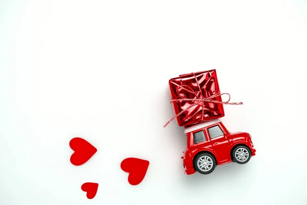 Valentines card with  little red toy car carrying red gift box and red hearts on a   white background