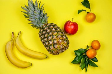 Üst manzara taze tropikal meyve düzeni ananas, muz, elma ve mandalina sarı arka planda.