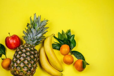 Üst manzara taze tropikal meyve düzeni ananas, muz, elma ve mandalina sarı arka planda.