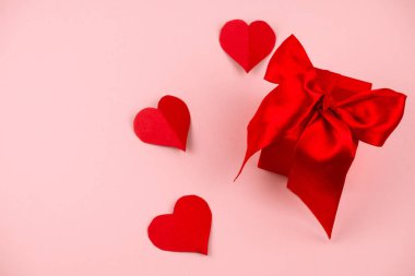 Kırmızı saten kurdeleli kırmızı hediye kutusu. Yay ve pembe arka planda kağıt kalpler.