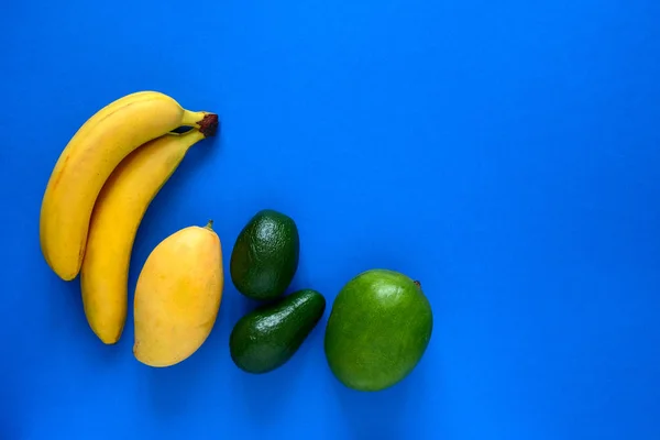 青い背景に新鮮なバナナマンゴーとアボカドのトップビューのレイアウトとテキストの場所 — ストック写真