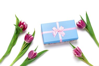 Üst mavi hediye kutusu, pembe yay ve beyaz arka planda izole laleler.