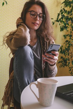Güzel beyaz kadın cep telefonu kullanıyor ve masada oturuyor.