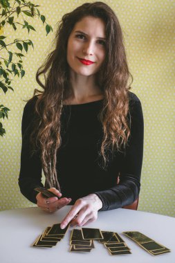 Siyah kadife elbiseli güzel, gülümseyen genç bir kadın masaya kartlarını serer.