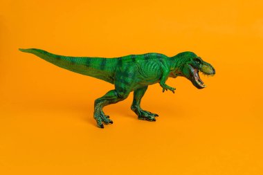 Canlı turuncu arka planda ağzı açık bir yeşil dinozor oyuncağı.