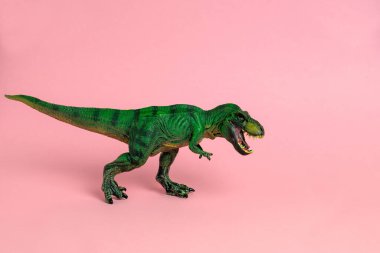 Pastel pembe arka planda ağzı açık yeşil dinozor oyuncağı.