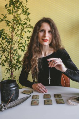 Tyumen, Rusya, 12 Şubat 2020. Siyah kadife elbiseli güzel bir kadın ruhani bir seans sırasında rünlerin üzerinde gümüş bir zincir tutuyor.