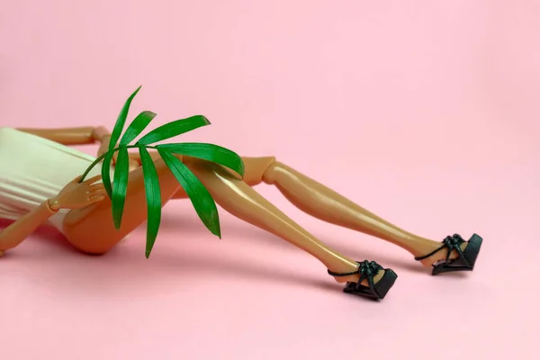 Close Plastic Doll Lying Pink Background Holding Palm Leaf Copy — Stock Photo, Image