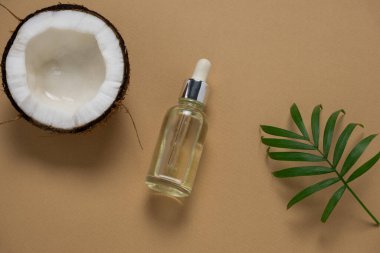 Üst görünüm kozmetik yağ şişesi, hindistan cevizi ve bej arka planda tropikal yaprak