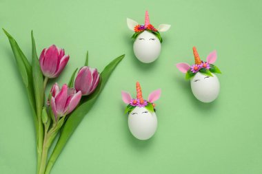 Yeşil arka planda şirin tek boynuzlu at yumurtaları ve pembe laleler, şirin asgari paskalya kartı.
