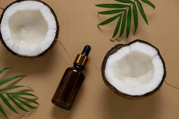 top view cosmetic oil bottle ,coconut and tropical leaf on a beige background