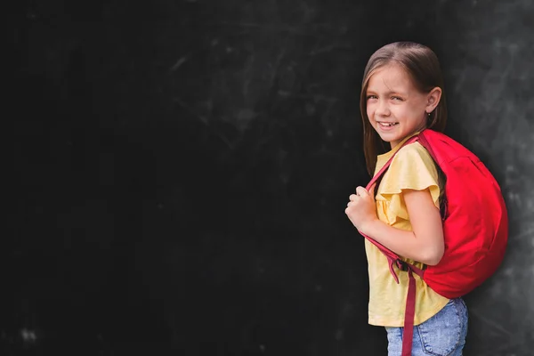 赤のバックパックを着た可愛い女の子が黒板に立ってテキストの場所に学校のコンセプトに戻る — ストック写真