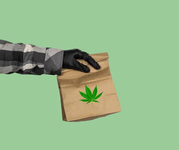 マリファナの配達の概念緑の背景に大麻の葉のパッケージと黒手袋の宅配便の手 — ストック写真