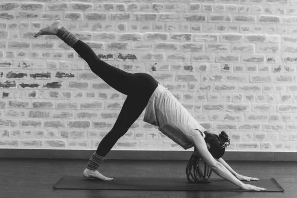 年轻女子在瑜伽垫上做瑜伽运动 与砖墙的黑白摄影相抗衡 — 图库照片