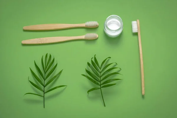 Bambu çevre dostu diş fırçaları, diş macunu kavanozu ve yeşil tropikal yapraklar, ev yapımı diş macunu ve diş bakımı konsepti.