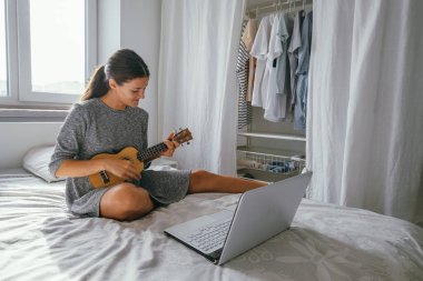 Güzel, genç bir kadın evde gitar çalmak için ders çalışıyor. Yatak odasındaki yatağın üzerinde bir defter var.
