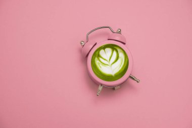 Pembe çalar saat içinde yeşil Japon kibrit çayı pastel pembe arka plan fotokopi alanı, detoks ve sağlıklı yaşam tarzı zaman kavramı.