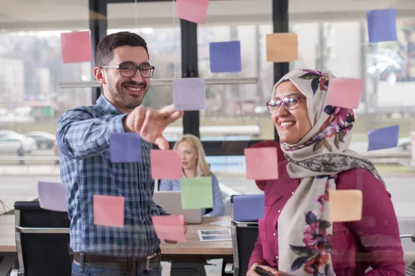 Compañeros de trabajo están discutiendo ideas sobre la pared de vidrio con stic — Foto de Stock