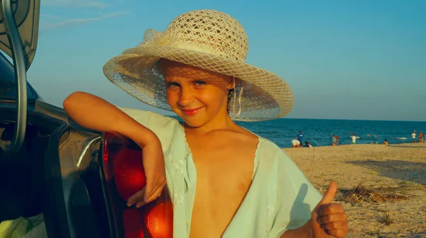漂亮的女孩在汽车附近的海滩上戴帽子 免版税图库图片