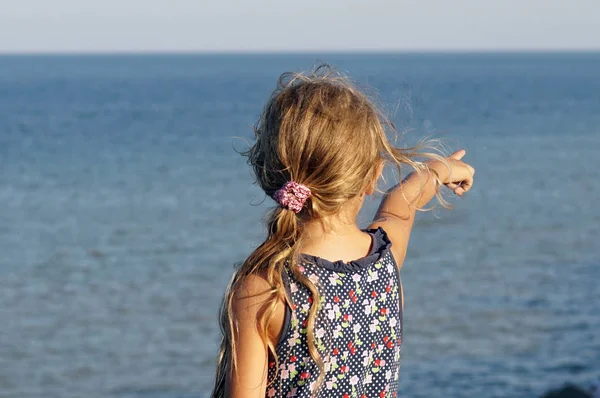 Klein meisje in gekleurde jurk wijst haar vinger op de zee — Stockfoto