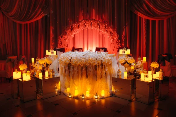 Table de mariage des jeunes mariés décorée avec des bougies et des lumières rouges derrière . — Photo