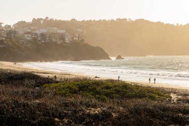 Golden Gate köprüsü yakınlarındaki Baker Sahili 'nde rüzgarlı bir gün, San Francisco, California. Gün batımından önce sıcak ışıkla sahilde yürüyen turistler.