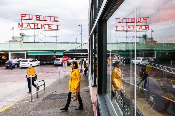 Seattle, Washington, USA - October 9, 2019: Young lady in yellow coat walking out from shop in public market of Pike Place market in Seattle, popular place for tourist in Seattle.