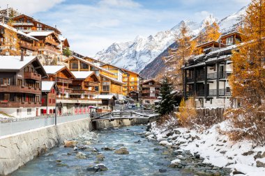 Zermatt, İsviçre - 11 Kasım 2019: Kışın karla kaplı ahşap evler ve tatil köyleriyle birlikte kayalık deresi olan eski bir kasabanın manzarası.