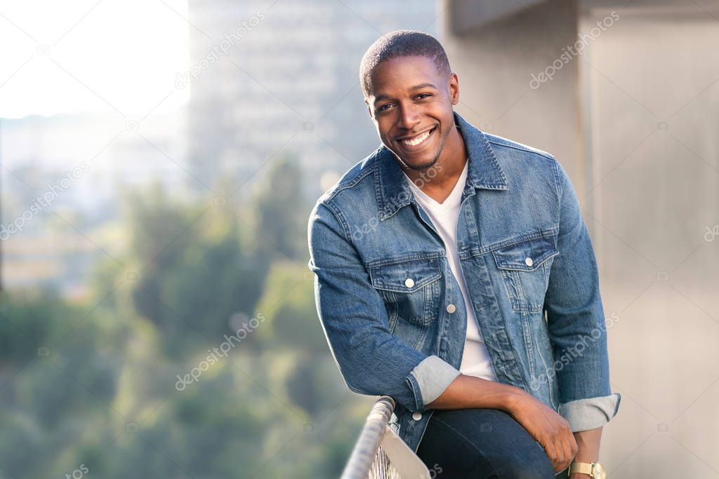 Relaxed and casual modern african american male portrait in blue jean jacket on a city rooftop during sunset