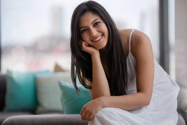 Cute adorable beautiful young Indian american woman at home sitting on sofa, smiling, cheerful, femininity, pretty face, portrait
