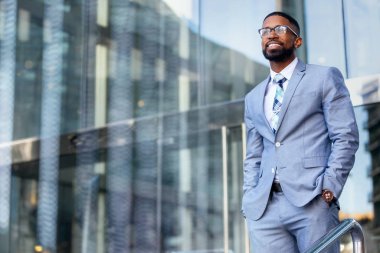 Genç başarılı Afro-Amerikan Ceo işletme kurucusu, şık takım elbiseli ve gözlüklü işyeri ofis binasında güvenle ayakta duruyor.