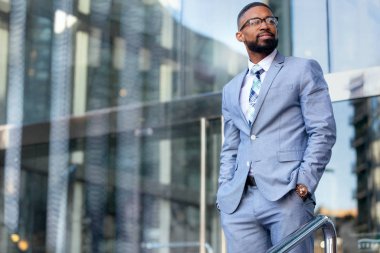Yakışıklı Afro-Amerikan iş adamı Ceo, şık bir takım elbiseyle işyerinin önünde güven içinde duruyor.