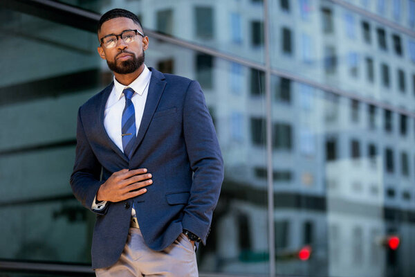 Proud successful businessman executive CEO african american, standing confidently with arms folded in downtown, financial buildings and skyscrapers