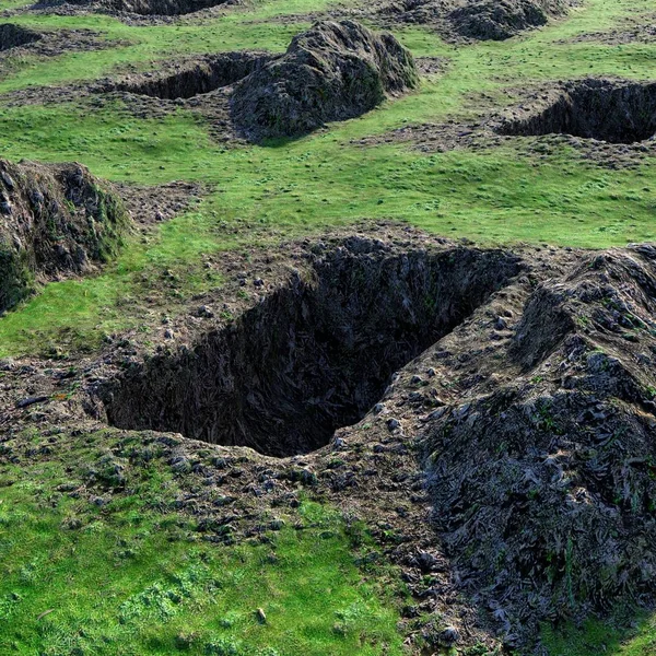 Kazılmış ve boş mezarları olan büyük bir tarla manzarası. Gün