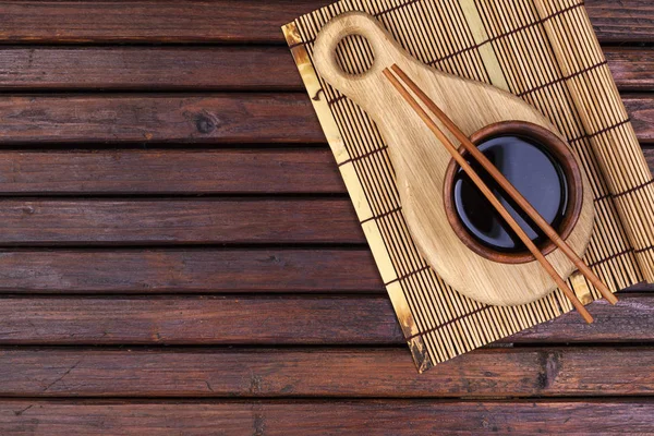 Pozadí pro sushi. Bambusová rohožka, sójová omáčka, hůlky na dřevěném stole. Horní pohled s mezerou pro kopírování — Stock fotografie