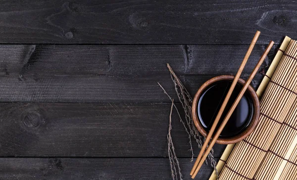 Pozadí pro sushi. Bambusová rohož, sójová omáčka, hůlky na tmavý stůl — Stock fotografie