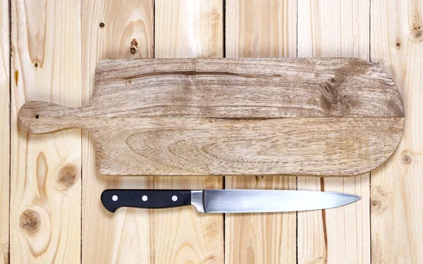 Cutting board with knife on wooden table. Top view