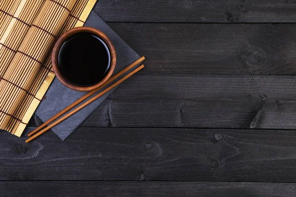 Bakgrunden för sushi. Bambu matta, soja, pinnar på mörka bord. Ovanifrån med kopia utrymme — Stockfoto