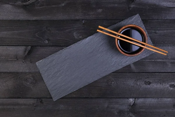 Accesorios para sushi. Salsa de soja, palillos en plato de piedra negra. Vista superior con espacio de copia — Foto de Stock