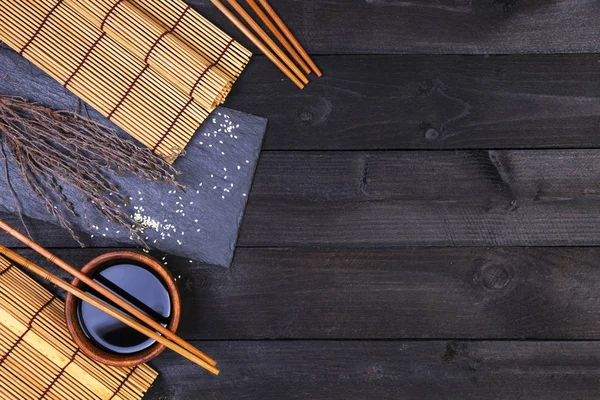 Antecedentes para sushi. Tapete de bambu e molho de soja na mesa de madeira preta. Vista superior com espaço de cópia — Fotografia de Stock